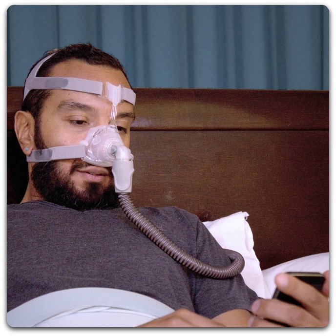 Man using phone in bed wearing PAP machine